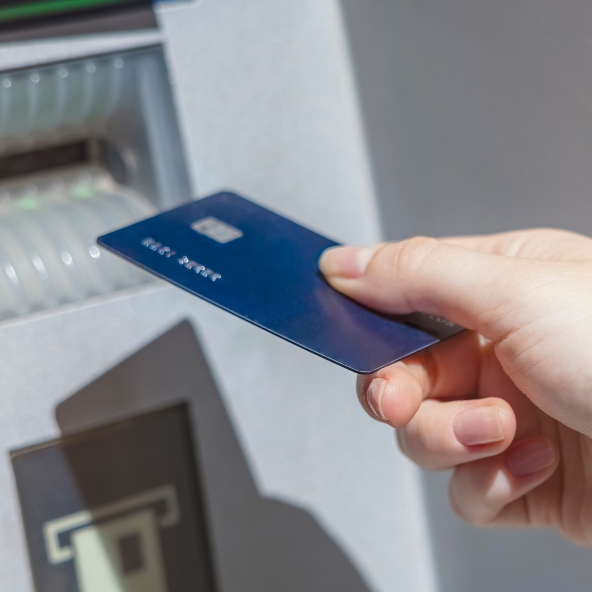 Zbliżenie na granatową kartę płatniczą, trzymaną w ręku przy bankomacie