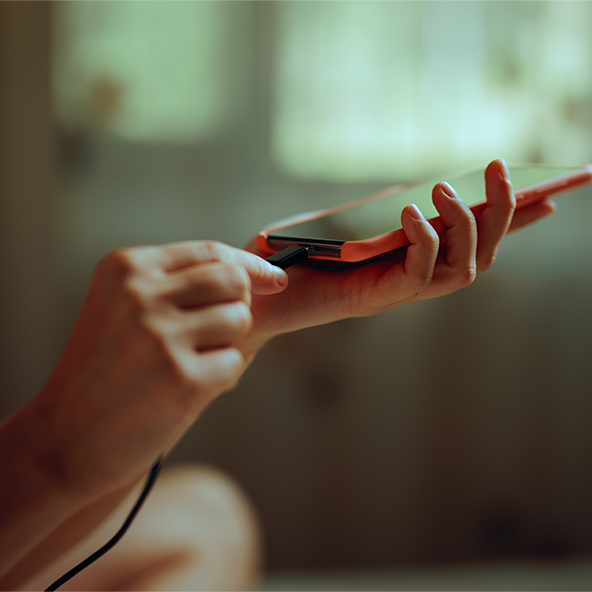 Obraz przedstawia kobiecą dłoń podłączającą kabel ładowarki do telefonu