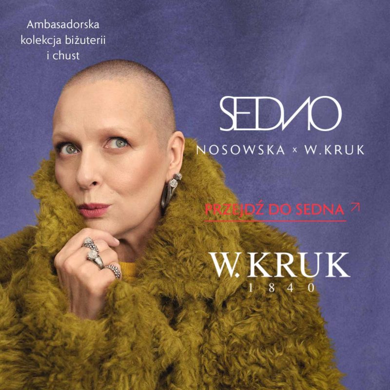 Katarzyna Nosowska w puszystym, oliwkowym okryciu prezentuje kolczyki i pierścionki w srebrnym kolorze, trzymając dłoń pod brodą. Na fioletowym tle napisy „SEDNO NOSOWSKA x W.KRUK”, „Ambasadorska kolekcja biżuterii i chust” oraz „Przejdź do SEDNA”, a także logo W.KRUK.